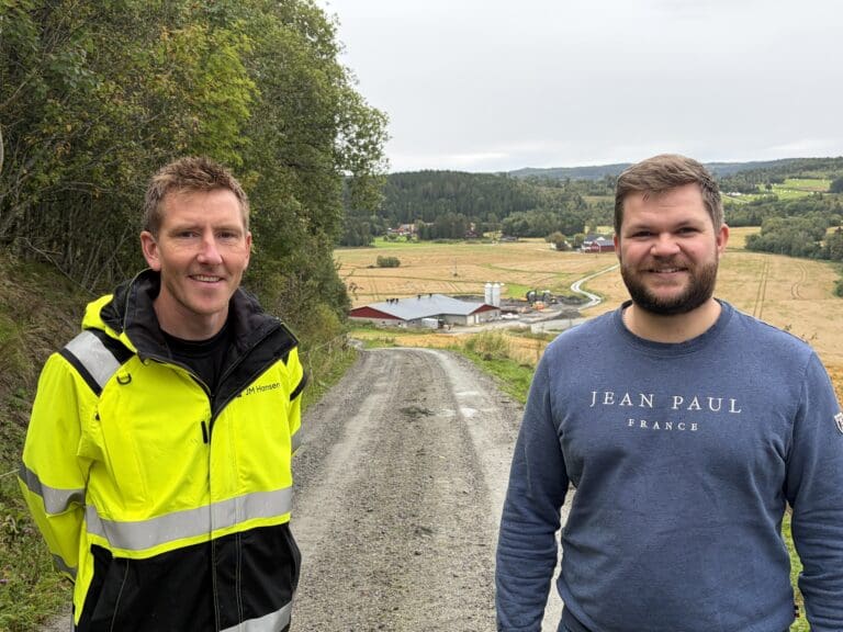 To menn står i en bakke. I bunnen av bakken ligger et fjøs.