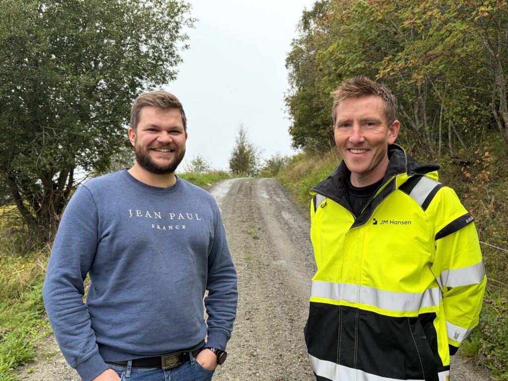 To smilende menn; en med arbeidsjakke med logoen til JM Hansen