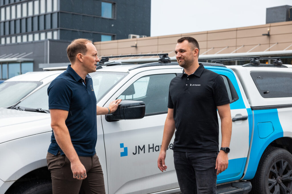 To menn i samtale ved en bil med JM Hansen-logoen