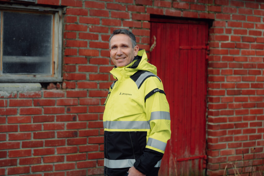 Smilende mann i gul arbeidsjakke med JM Hansen på
